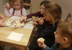 dzieci siedzą przy stolikach, jedzą ciasteczka